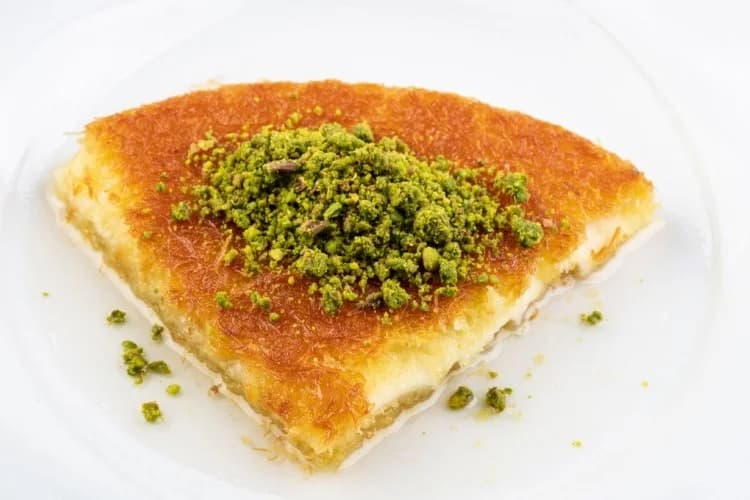 Palestinian knafeh Nabulsi with a golden semolina crust, crushed pistachios, and a soft cheese filling.